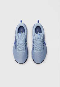 Een paar lichtblauwe Nike Pegasus Trail hardloopschoenen met mesh bovenwerk en veters, gezien van bovenaf op een witte achtergrond.