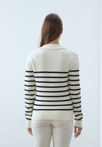 Knit sweater in cream with horizontal black stripes. Features a ribbed texture and collar, long sleeves, and fitted hem.
