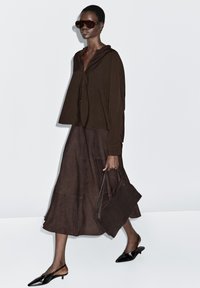 Brun knap-up skjorte og flagrende midi nederdel, parret med sorte slingback sko og en matchende håndtaske; glat stof med en blød tekstur.