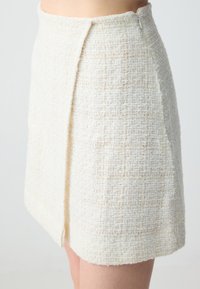 Jupe mini en tweed blanc avec un motif texturé, dotée d'une fermeture éclair sur le côté et d'une silhouette légèrement évasée.