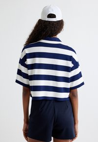 Affodret polo shirt med vandrette navy og hvide striber, korteærmer, en moderne krave og en ensfarvet søm. Sammen med mørke shorts.