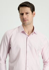 Helles rosa Hemd mit Knopfleiste, das dünne weiße Streifen aufweist, einen Spread-Kragen hat und lange Ärmel mit geknöpften Manschetten besitzt.