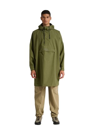 Olivengrøn vandtæt poncho med en frontlomme, justerbar hætte og snore. Kombineret med beige bukser og sorte sko.