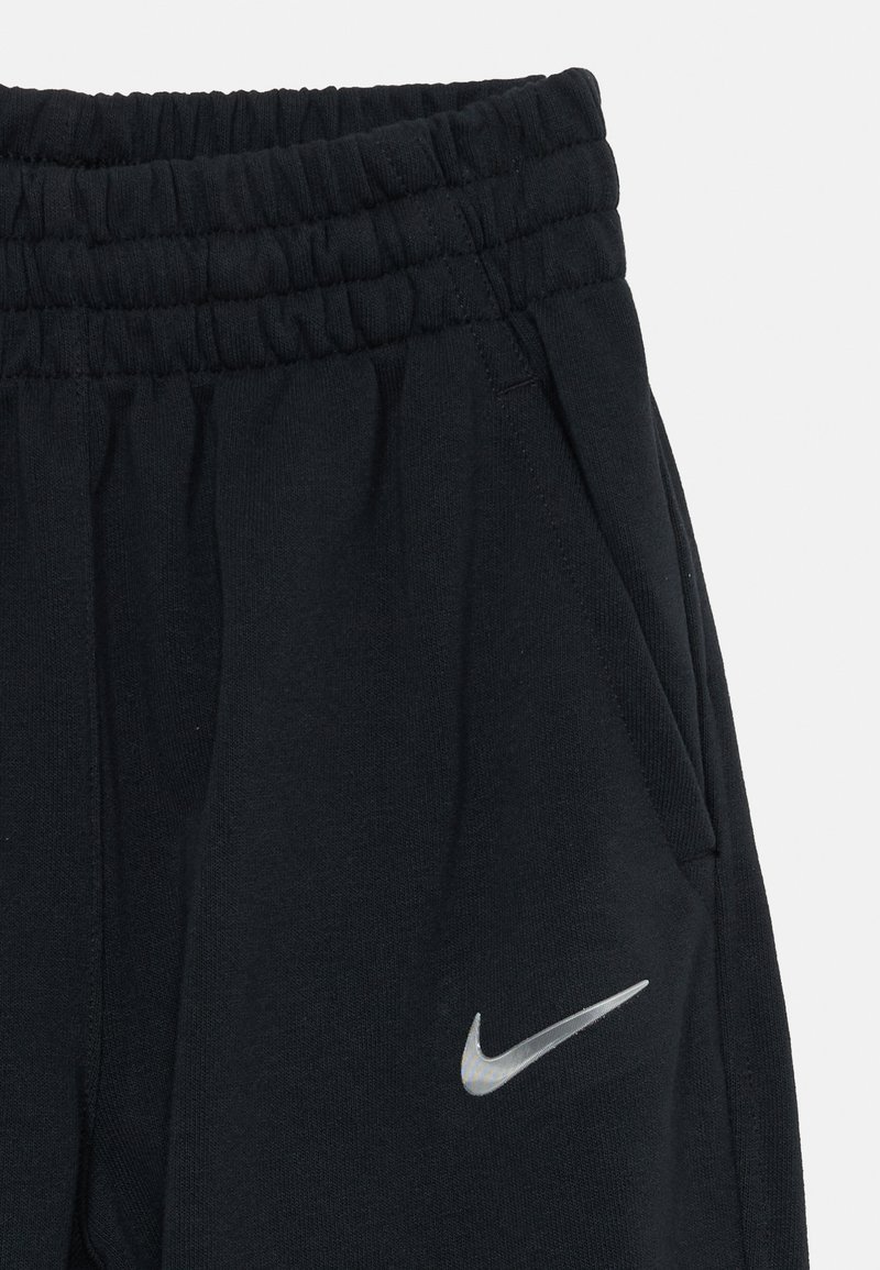 Pantalones deportivos negros con cintura elástica, bolsillos laterales y un logo reflectante de Nike en el muslo izquierdo. Tejido suave de mezcla de algodón.