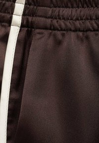Tissu marron foncé avec une texture lisse et un léger éclat, présentant une bande blanche sur le côté et des détails d'élastique à la taille.