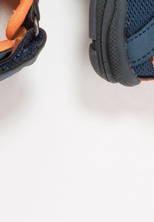 Chaussures bleu marine avec des accents orange, présentant une tige texturée, une semelle en caoutchouc et une bride à boucle auto-agrippante pour un maintien sécurisé.