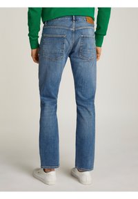 Modré denimové džíny se středně širokým střihem, dvěma zadními kapsami a hnědou koženou nášivkou na pase. Nosené s bílými teniskami.