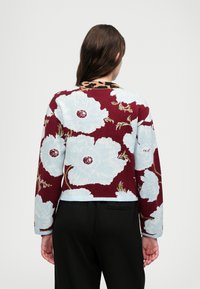 Pulôver de malha com uma base em bordeaux e grandes padrões florais em azul claro. O design inclui uma bainha canelada e um colarinho com padrão de leopardo.