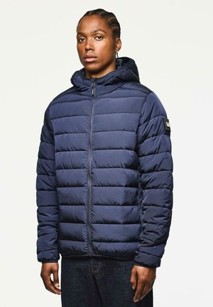 Navy blue puffer jacket with a zip closure, horizontal stitching, and a hood. Features ribbed cuffs and a logo patch on the left shoulder.