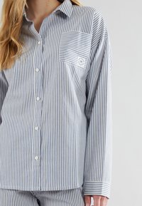 Camicia a righe in cotone blu e bianco con taschino e un piccolo logo. Presenta maniche lunghe e colletto classico.