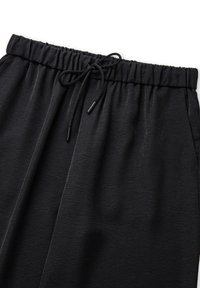 Zwarte joggerbroeken met een gestructureerd oppervlak, elastische tailleband en verstelbaar trekkoord. Voorzien van zijzakken en een relaxte pasvorm.