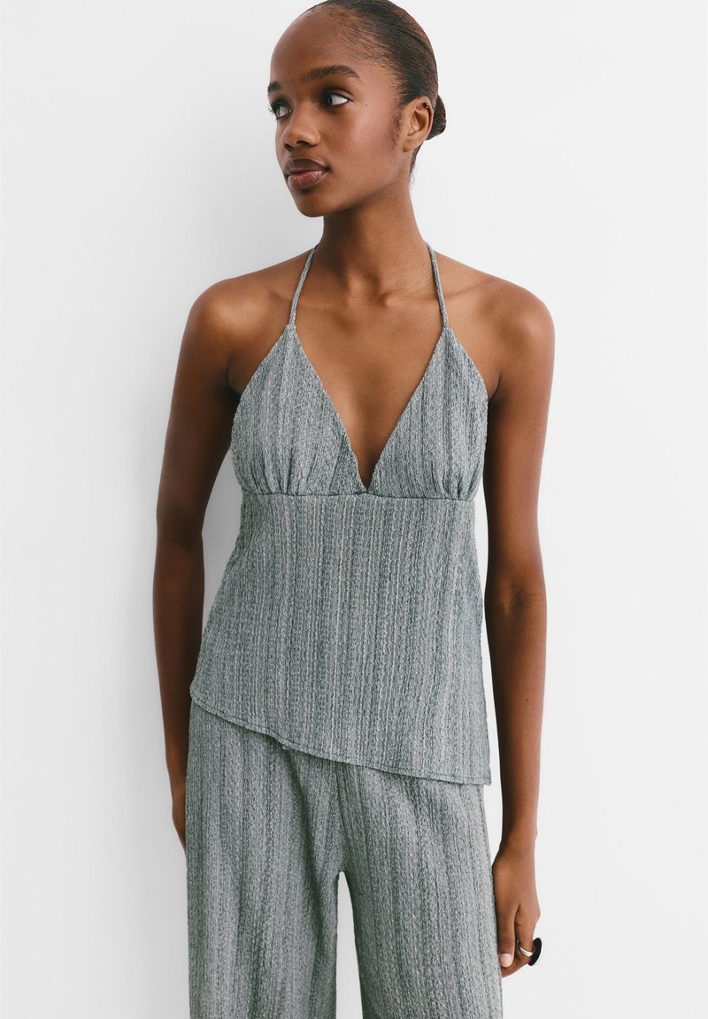 Siva halter top s V-izrezom, teksturirana tkanina s vertikalnim prugama i višeslojnim rubom, u kombinaciji s odgovarajućim teksturiranim hlačama.