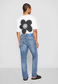 White t-shirt featuring a large black flower graphic on the back, paired with light blue jeans and black footwear. cotton blend material.