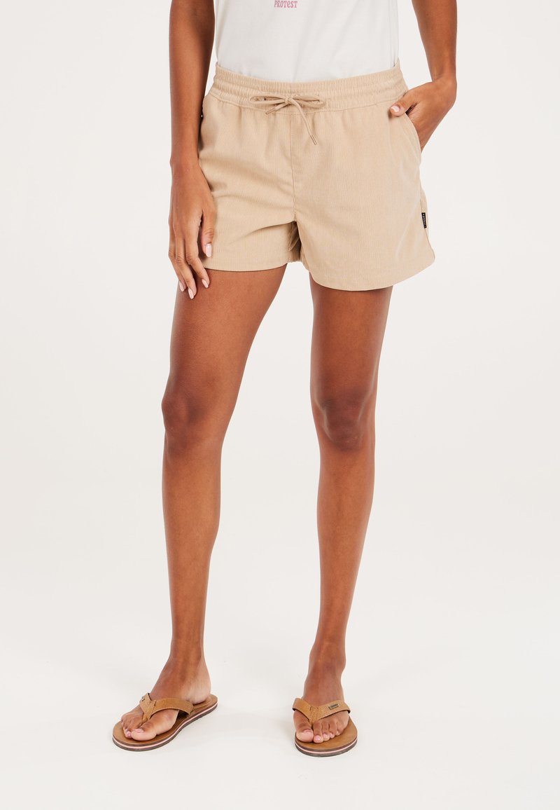 Beige shorts met een elastische tailleband en trekkoord, voorzien van subtiele verticale strepen en zijzakken. Draag met bruine slippers.