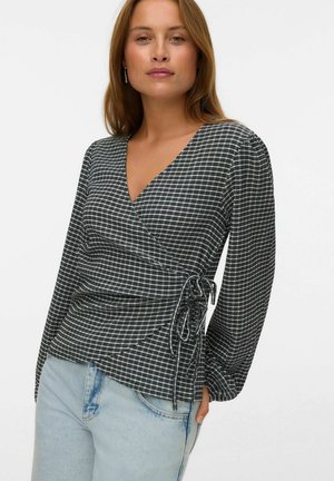 Black and white checkered wrap top with long sleeves, featuring a tied accent on the side and a textured fabric. Paired with light blue jeans.
