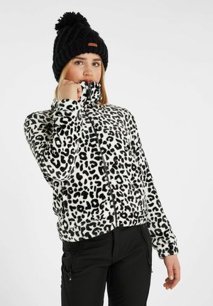 Veste en polaire avec un imprimé léopard noir et blanc, col haut, fermeture éclair devant et accents noirs. Portée avec un bonnet en tricot noir.