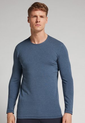 T-shirt à manches longues et col rond en tissu texturé bleu foncé, arborant une coupe ajustée et des coutures discrètes le long de l'encolure et des poignets.