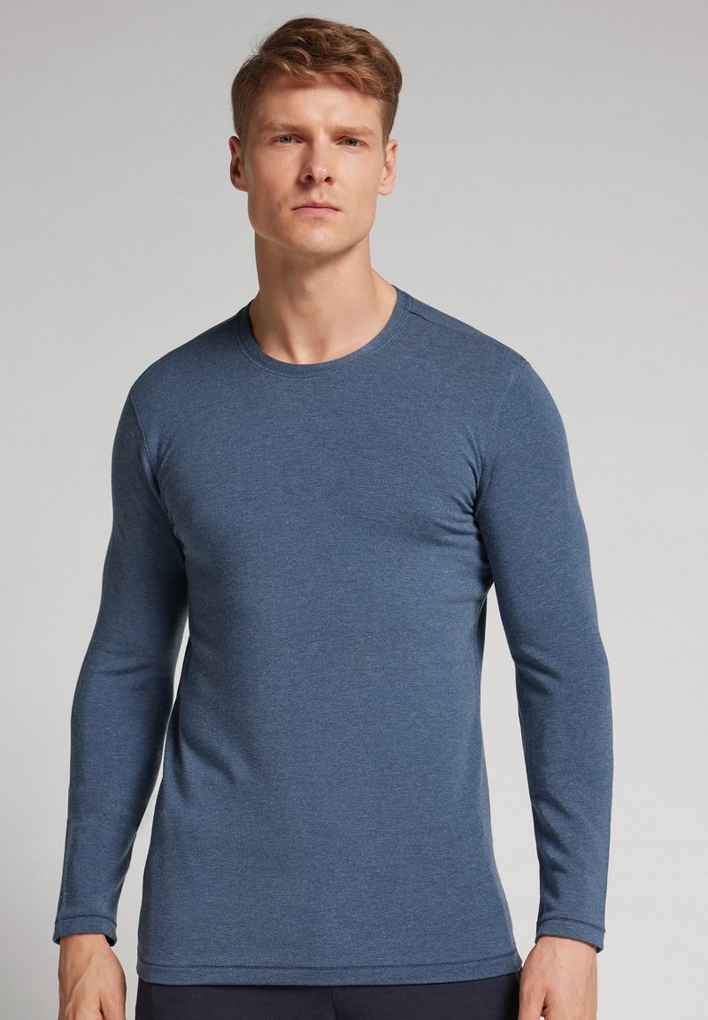 Dlouhý rukáv tričko s kulatým výstřihem v texturované tmavě modré tkanině, s přiléhavým střihem a jemným prošitím podél výstřihu a manžet.