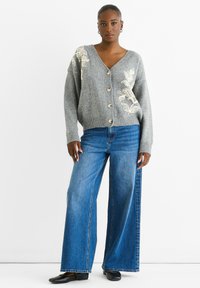 Gray knitted cardigan with floral embroidery, wide sleeves, and buttons. Paired with high-waisted blue wide-leg jeans and black flats.