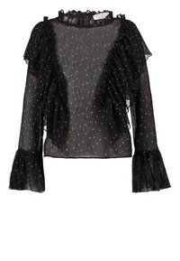 Blouse noire transparente à pois blancs, finition à volants sur le devant et aux poignets, manches longues, col haut avec détail volanté.