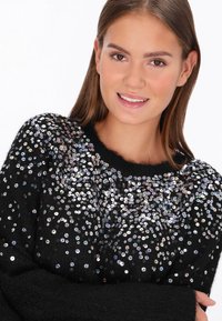 Fekete pulóver, texturált kötött anyaggal, színes flitterekkel szétszórva, kerek nyakkivágással és bordás mandzsettával.