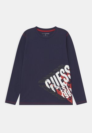 Marineblå T-shirt med lange ærmer i bomuld, har et rødt grafisk design med "GUESS" og "est. 1981," kontrastsyet langs ærmerne.