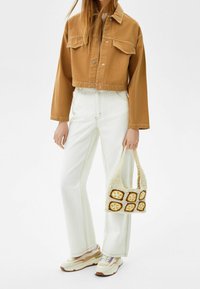 Avskuren brun denimjacka, vita högmidjade jeans, beige virkade väska med kvadratmönster och färgglada klumpiga sneakers.