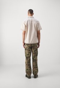 Beige overhemd met korte mouwen en een kraag, gecombineerd met groene camouflage cargobroek met zijzakken en een relaxte pasvorm.