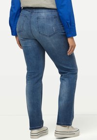 Blå denimjeans med slim fit, med medelhög midja, två bakfickor och fransad nederkant, tillsammans med vita sneakers.