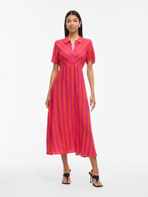 Robe chemise rayée rose et orange avec des manches courtes, une silhouette fluide et une coupe mi-longue. Des sandales à talons noires complètent le look.
