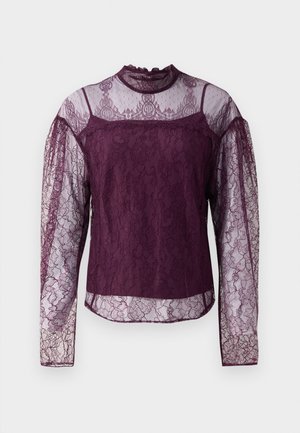 Purppuranvärinen pitsi pitkähihaisessa puserossa on läpinäkyvät osat hihoissa ja ylärinnassa, jossa on korkea kaula-aukko ja monimutkaiset kukkakuviot.
