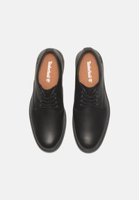 Scarpe in pelle nera con finitura liscia, forma a punta rotonda, cuciture a contrasto, design con lacci e soletta marrone con logo.