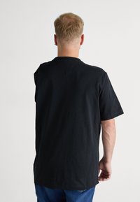 Crna majica kratkih rukava od pamuka, s okruglim izrezom i ravnim rubom te opuštenim krojem. Nema vidljivih uzoraka ili naglasaka.