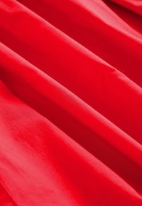 Tela roja con textura suave, que presenta múltiples caídas y pliegues suaves, exhibiendo un color rico y uniforme.