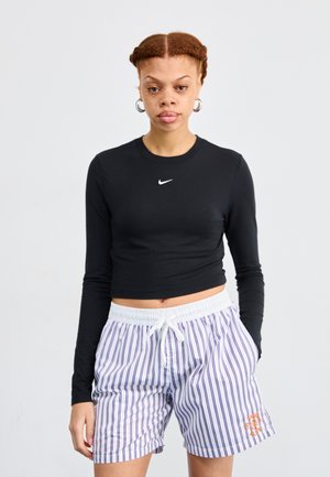 Crop top nero a maniche lunghe con logo bianco, abbinato a pantaloni corti bianchi con strisce viola e dettagli grafici arancioni sul lato.
