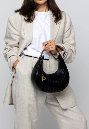 Black pleated leather handbag with a gold hardware accent and zipper, held by a person wearing a beige suit and a white shirt.