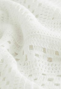 Suave tela de ganchillo blanca con patrones cuadrados y costuras texturizadas, doblada suavemente para mostrar profundidad y detalle.