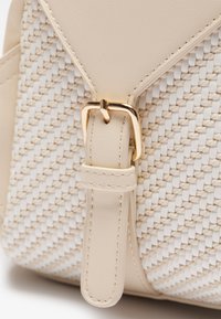 Beżowa torebka z plecionym wzorem i gładkimi skórzanymi akcentami. Złote okucia i detal w postaci klamry podkreślają jej kształt.
