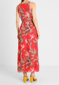 Rød maxi-kjole med blomstermønster, der har farverige blade og blomster. Letvægtsstof, ærmeløs design og en flydende silhuet.