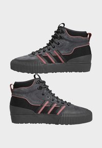 Zapatillas altas con parte superior de ante gris y textil negro, con rayas marrón, cordones negros y una suela de goma negra sólida y estriada.