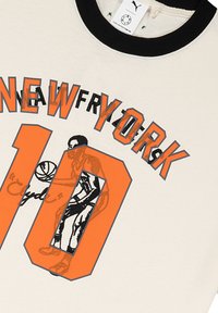 Vit T-shirt med svart ribbad krage som har en orange grafik med texten "NEW YORK 10" och en spelare som håller en basketboll.