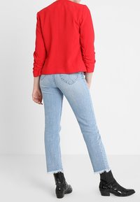 Blazer rosso attillato con maniche arricciate, abbinato a jeans azzurri a gamba dritta con orli sfrangiati e stivaletti neri alla caviglia.