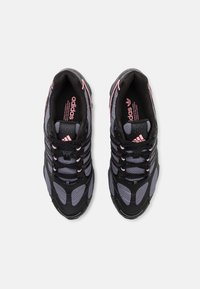 Scarpe da ginnastica nere e grigie con tomaia in mesh, dettagli rosa e suola testurizzata; presentano lacci e il marchio Adidas sulla soletta.