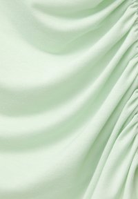 Lichtgroene stof met een zachte, gladde textuur, gekenmerkt door zachte plooien en geraffineerde details aan één kant. Duurzaam, rekbaar materiaal.