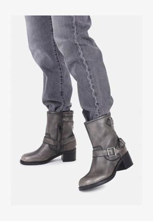 Pelēkas ādas potītes zābaki ar nedaudz spīdīgu apdari, masīviem melniem papēžiem, sānu rāvējslēdzēju un dekoratīvām siksnām ar sprādzēm.