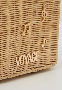 Gros plan d'une surface en osier tissé décorée de notes de musique dorées et du mot "VOYAGE" en lettres dorées.