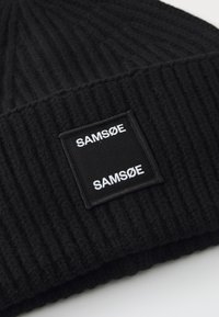 Berretto lavorato a maglia nero caratterizzato da una texture a coste e un'etichetta quadrata nera con testo bianco "SAMØSØ" sul davanti.