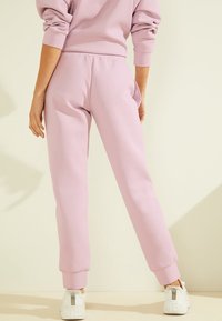 Světle růžové tepláky s volným střihem, elastickým pasem a žebrovanými manžetami, doplněné bílými teniskami s detailem loga.