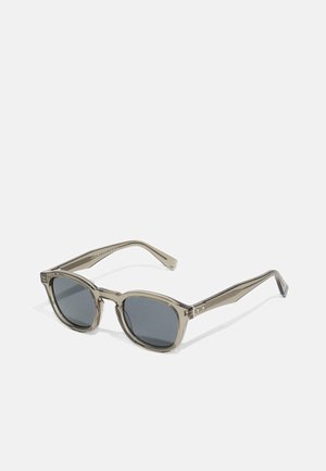Sonnenbrille mit einem durchsichtigen grauen Rahmen, runden Gläsern und dunkler grauer Tönung. Die Bügel haben ein dezentes Designmuster und silberne Akzente.