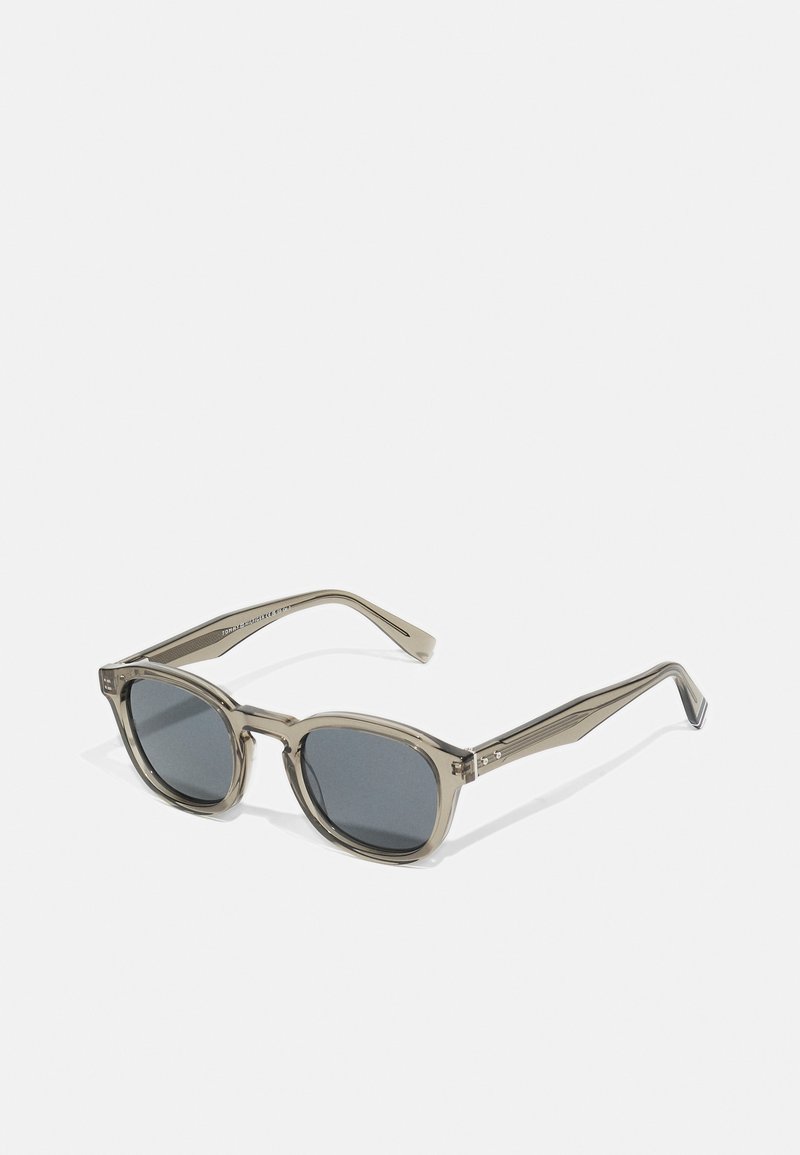 Sonnenbrille mit einem durchsichtigen grauen Rahmen, runden Gläsern und dunkler grauer Tönung. Die Bügel haben ein dezentes Designmuster und silberne Akzente.